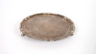 A silver card tray, having shaped border raised on three hoof feet, Sheffield 1936, 21cm dia., 254.