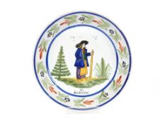A Quimper type shallow dish, decorated with a farm worker carrying a staff, inscribed 'Auvergne' and