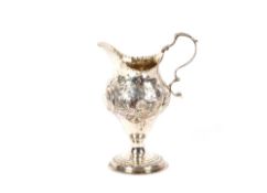 A George III silver helmet shaped cream jug, having foliate scroll decoration and monogrammed