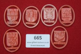 A group of six red celluloid day badges, each bearing the crest and name of a city or town,
