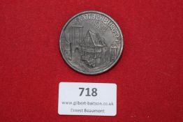 Circular aluminium tinnie depicting medieval town buildings, inscribed Rothenburg 1938. Reverse