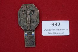 A bronze event badge depicting an athletic figure with barbell, inset with blue and white enamel and