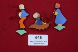 Three painted wooden figures, linked with cord, depicting children in traditional dress, one pulling