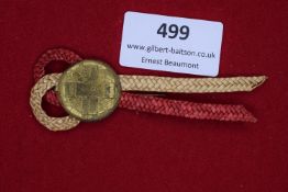 A woven straw-work badge with red and cream braid, mounted with a circular gilt tinnie dated 1936,