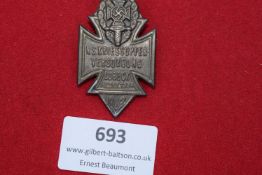 A pressed tin badge in the form of a cross, surmounted by a sword and wreath with swastika,