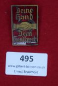 A rectangular gilt and red enamel-finished badge, with two clasped hands over swastikas, inscribed