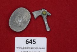 Two badges, one oval shield-form with rivet design, the other a battle axe with yellow-green stone