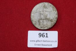 A circular alloy festival badge showing an athletic figure with laurel wreath. Reverse stamped E.
