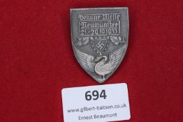 A shield-shaped event badge showing a swan beneath a shield with swastika, inscribed “Braune Messe