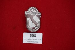 A die-stamped tinnie badge in silvered finish, showing the map of Italy below cogwheel and swastika,