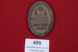 An oval pressed metal badge featuring Lübeck’s Holstentor with swastika above, inscribed around “