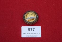 Souvenir brooch-style badge with looped gilt border, showing a celluloid insert image inscribed 