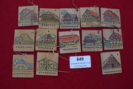Twelve small wooden plaques, each painted with regional German architectural styles including