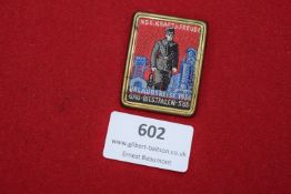 A scarce rectangular cloth and metal-framed badge in coloured embroidery, showing a uniformed figure