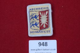 A colourful woven cloth and metal-framed event badge for the Heimatfest held at Aschberg,