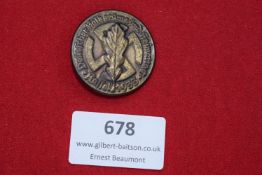 A circular bronze-coloured badge with central oak leaf over swastika, surrounded by inscription “