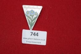 A triangular aluminium badge with enamelled blue and yellow forget-me-not flowers, inscribed 