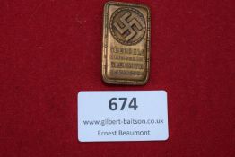 A rectangular bronze-coloured rally badge, featuring a prominent swastika within a circular