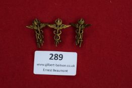 Three German medical qualification badges, brass construction with crown, winged staff, and serpent