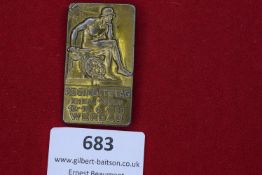 A large rectangular brass badge with figure of a seated soldier in helmet, swastika to upper corner,