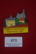 A German WWII WHW painted wooden day badge, in the form of a townscape, inscribed “Volks- u.