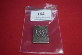 A German commemorative tinnie, rectangular form with crenellated top, depicting marching soldiers