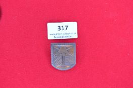 Shield-Shaped Commemorative Badge – A bronzed pressed metal badge depicting a central German