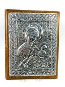A Russian cast silvered metal Icon with Cyrillic script, mounted upon a wooden backboard