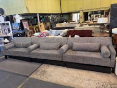 A large, modern sectional sofa in a grey, textured fabric The sofa is composed of three individual s