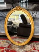 Ornate oval mirror makes a captivating statement. Its frame, finished in a luxurious gold leaf or