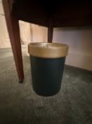 A cylindrical wastebasket or bin features a dark green body with a contrasting golden or brass-toned