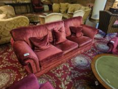 A classic three-seater sofa, upholstered in a rich red velvet-like fabric, featuring rolled arms,