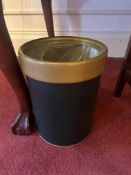 A cylindrical waste bin, featuring a main body of dark, likely black-painted composite. It is