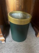 A cylindrical waste bin with a simple, modern design. It features a dark green painted metal body,
