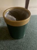 A cylindrical wastebasket or bin features a dark green body with a contrasting golden or brass-toned