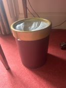 A cylindrical wastebasket or bin features a dark red body with a contrasting golden or brass-toned
