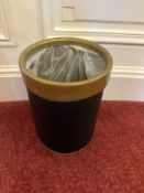 A cylindrical wastebasket or bin features a dark green body with a contrasting golden or brass-toned
