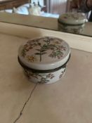 A white glazed porcelain lidded box in the Staffordshire Enamels style. Circular in form with a