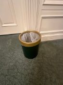 A cylindrical wastebasket or bin features a dark green body with a contrasting golden or brass-toned
