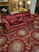 A classic three-seater sofa, upholstered in a rich red velvet-like fabric, featuring rolled arms,