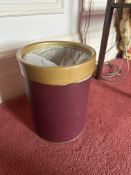 A cylindrical wastebasket or bin features a dark red body with a contrasting golden or brass-toned