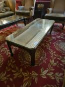 A Rectangular cocktail table with a clear, protective glass top resting over a wooden surface. The