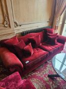 A classic camel back upholstered sofa in deep red velour upholstery gently scrolled back and
