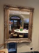 A large, rectangular mirror with an ornate, giltwood frame. The frame features intricate
