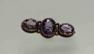 An Edwardian yellow metal three stone oval faceted amethyst brooch in rope pattern border the center