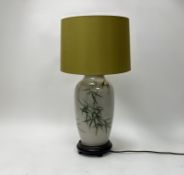 A modern ceramic table lamp decorated with bamboo leaves, raised on an ebonised wooden stand,
