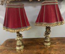A pair of cast brass table lamps in the Rococo style, with putti and foliate detail and red