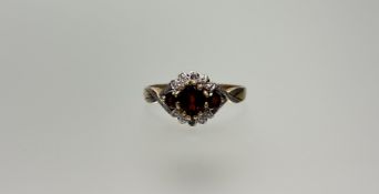 A 9ct gold ring set oval red cut stone flanked by a circular stone to each shoulder in white metal