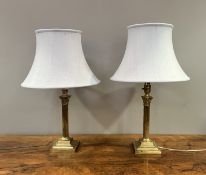 A near-matched pair of brass table lamps of corinthian form, raised on stepped bases, complete