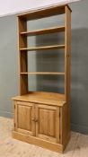 A modern pine open bookcase, with three adjustable shelves to top, over a cupboard base, with twin